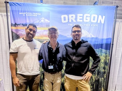 Three people face the camera and smile, standing in front of a large banner that says "Oregon: The sprawl free sate."