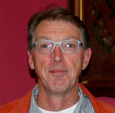 Ben Williams looks at the camera, wearing glasses, against a dark red background