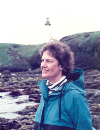 A younger Nancie Peacocke Fadeley stands on a rocky shorelines with a lighthouse in the background
