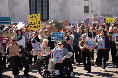 A large group holds up signs in front of the Salem capitol building