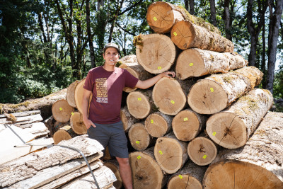 A man standing next to a stack of logs in a forested setting