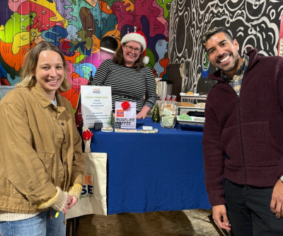 Three smiling people at an indoor market, next to a colorful mural