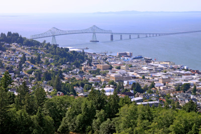 Aerial photo of Astoria, showing forested hillsides (with a smattering of homes) and a more densely developed waterfront area. There is also the Astoria-Megler Bridge spanning the wide Columbia River.
