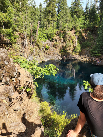 A person sitting on the edge of a crater filled with turquoise blue water