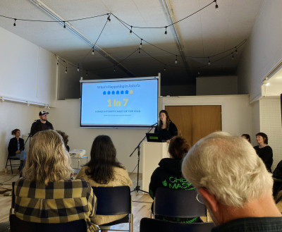 Two people standing in front of a large crowd, with a screen that reads, "1 in 7 homes sit empty every year."