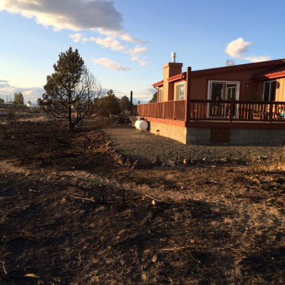 A home surrounded by burnt ground and burnt vegetation. The home itself looks untouched, and it has a border of gravel with no vegetation around it (defensible space).