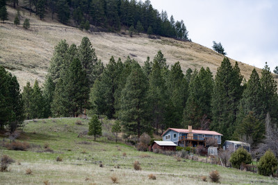 A large house with a red roof and chimney, on an arid, semi-forested hillside.