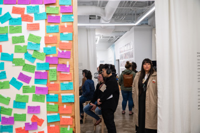 A group of people in an indoor, interactive art exhibit with colorful sticky notes on the left wall