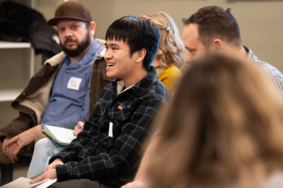 A smiling man talks in a group setting indoors