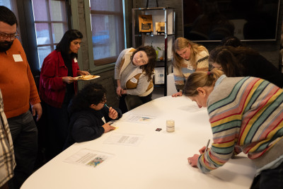 A group of people look at some documents on a table, including a woman leaning to the side
