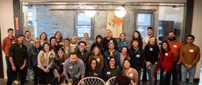 A group of smiling people in a modern office setting with art on the distressed brick walls