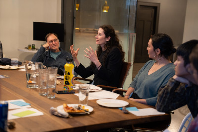 A woman gesturing with her hands during a conversation with a group seated around a wooden table