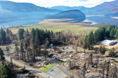 Aerial view of a picturesque mountain lake in the background, and a charred town in the foreground (Detroit, Oregon)