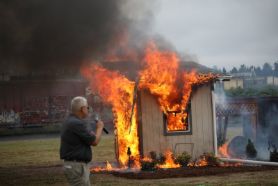 A model home burning, as a man looks on