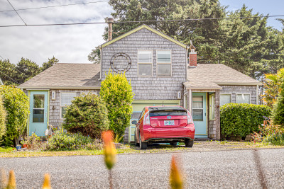 A duplex with weathered gray siding, pale blue doors, and a red car parked out front