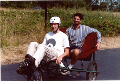 Two men on a pedal-cab, one pedaling and one riding in the cart