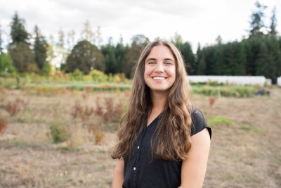 A smiling woman with long brown hair and a black shirt, in a rural setting