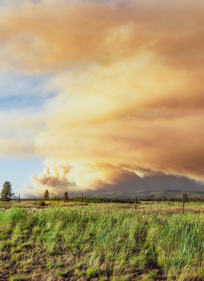 A wide open field and hazy smoke rising in the distance