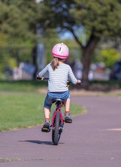 Child rides a bike on a path in a grassy park