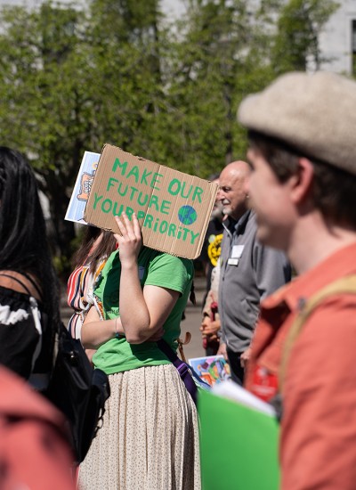 In a crowd at a rally, one person holds up a sign that says, "Make our future your priority"