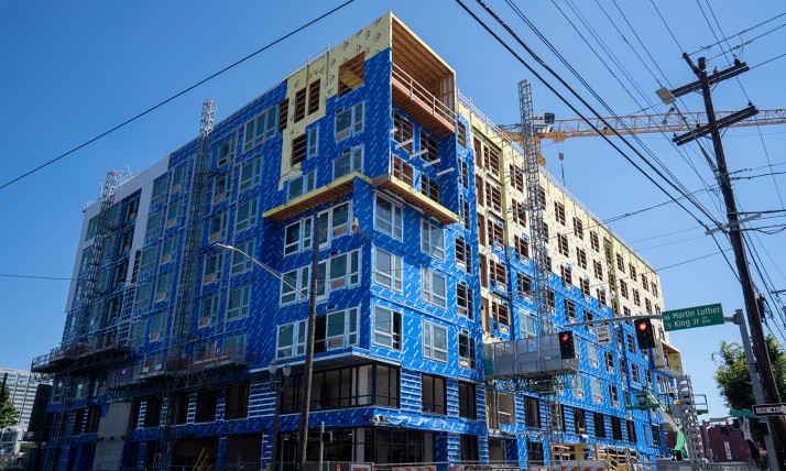 Multistory apartment building under construction in Portland. The building is wrapped in blue protective sheathing and siding is not yet installed.