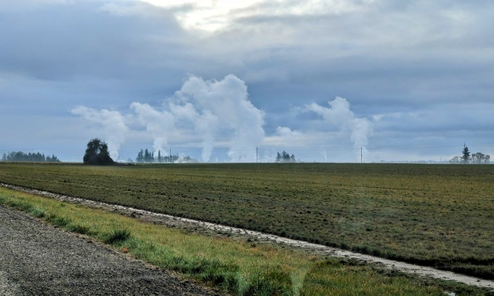 White vapor rises from ground level in the distance, looking over an open green field