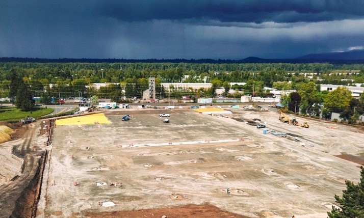 An overhead view of a leveled construction site. The ground is mostly dirt with some concrete footings spaced throughout the site.