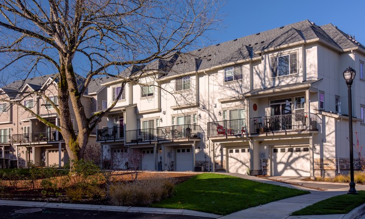 Multi-family housing in a neighborhood, with a green lawn and large tree