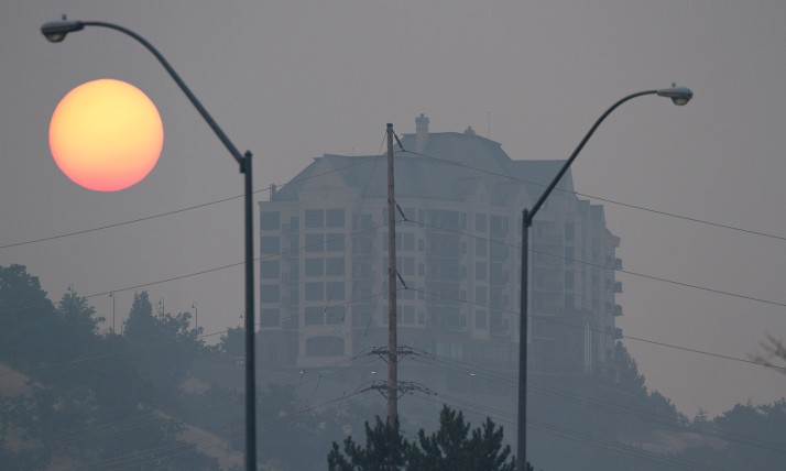 Heavy gray wildfire smoke obscures a view of Medford's Rogue Valley Manor, with a dimmed sun behind it.