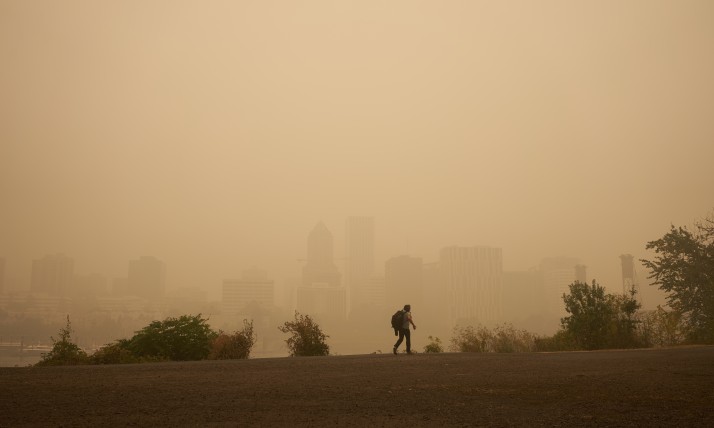 A person walking in front of the Portland skyline obscured by thick wildfire smoke