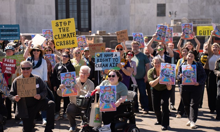 A large group holds up signs in front of the Salem capitol building