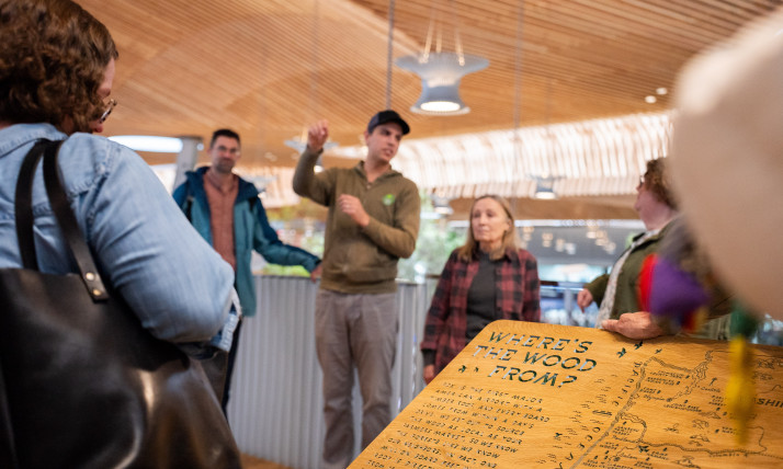A group of people in the newly-remodeled Portland International Airport, which has arcing wood ceilings. In the foreground of this shot is a map that shows where the wood is sourced from; the map shows Oregon and Washington locations including Zena Forest Products.