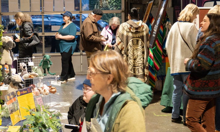 A crowd of people in an indoor market, with colorful booths and colorful murals on the walls.