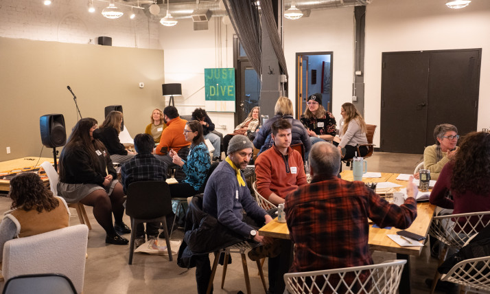 A group of people seated at tables, talking, in an indoor setting
