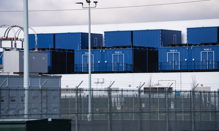 Blue, box-like buildings (data center) behind a barbed wire fence