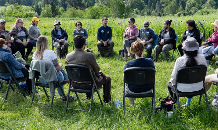 A group of people seated in a circle in a grassy field