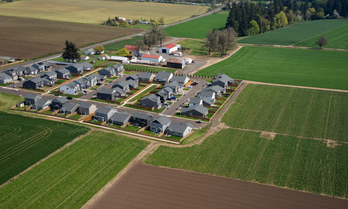 Aerial view of a compact town with many homes. This town has a clear rectangular edge, which then gives way to many hues of agricultural fields extending in all directions.