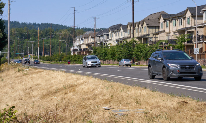 Cars driving down a straight road that runs parallel to a long line of townhomes