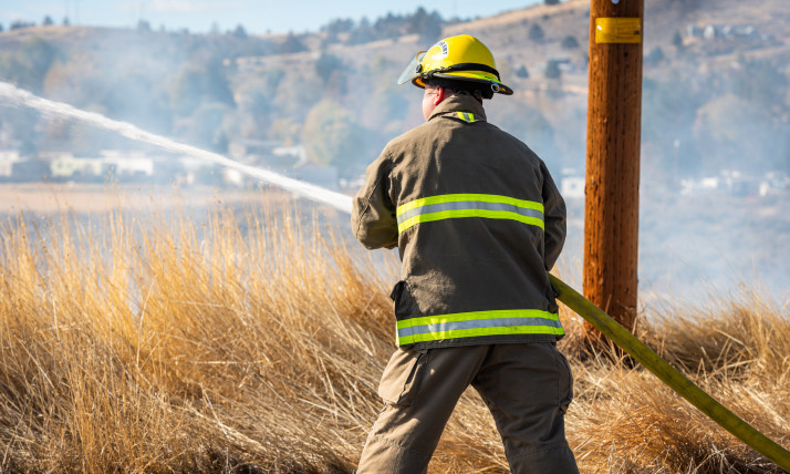 Back of a firefighter spraying a hose on a dry brown field