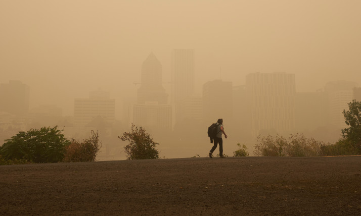 A person walking in a thickly hazy, orange-hued cityscape (Portland Oregon downtown)