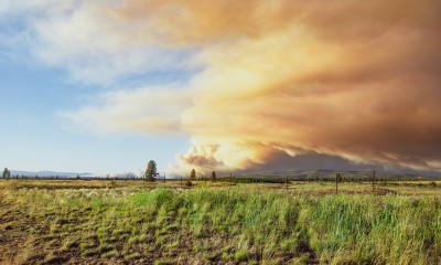 A wide open field and hazy smoke rising in the distance