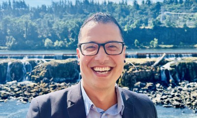 Justin stands outside with Multnomah Falls in the background and smiles at the camera on a sunny day