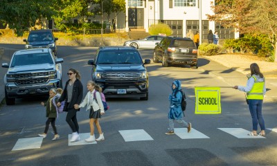 Children walk on a crosswalk with the help of an adult crossing guard. A car waits for them.
