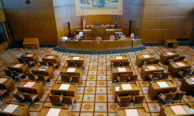 Interior of the Oregon legislative chamber, with rows of wooden desks on a tiled floor featuring alternating images of fish and wheat.