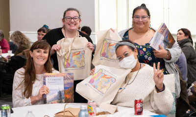 A group of four people smiling and posing with soil map tote bags and books in hand