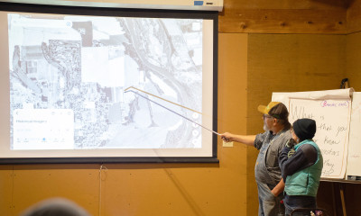 Two people stand in front of a room, pointing to a screen where historic maps of agricultural land are shown