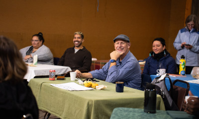 A group of people seated at long, forward-facing tables in an indoor setting