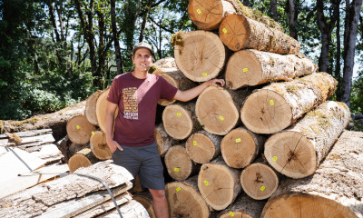 A man standing next to a stack of logs in a forested setting