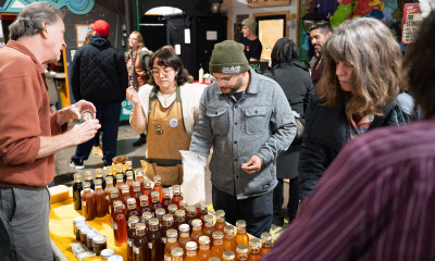 Two people visit a booth with many bottles of various-colored honey
