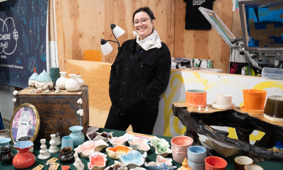 A woman smiles, standing at a table with a colorful ceramics display